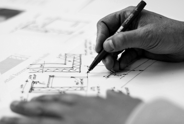 Hand holding black pen sketching building designs